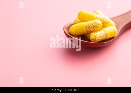 Vitaminkapseln. Vitamin-C-Pillen in Holzlöffel auf pinkfarbenem Hintergrund. Stockfoto