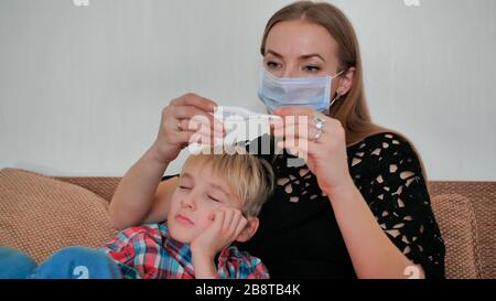 Eine fürsorgliche Mutter in einem Verband misst die Temperatur ihres Sohnes. Stockfoto