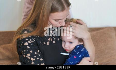 Die pflegende Mutter in einem Verband misst die Temperatur ihrer Tochter. Stockfoto