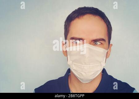 Ein junger Mann in einer weißen medizinischen Atemschutzmaske blickt weg. An der Grippe erkrankt. Schutz vor Keimen. Nachdenklicher Patient. Stockfoto