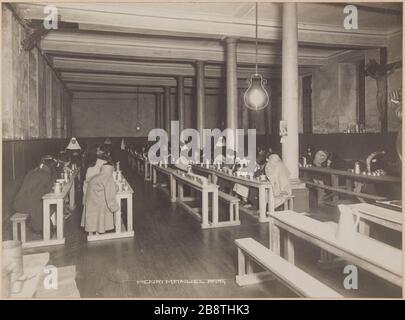 Im Refektorium festgehalten, das ihr Gesicht vor den eisernen Schalen verbarg, sind drei Schwestern Marie-Josefs Aufseherin. Anwesenheit auf einem Tisch rechts von einer Fotogrohe, die mit einer Kamera auf einem Tisch montiert ist (siehe Foto CARPH038251 / 31 Détenues au Réfectoire se cachant le visage, devant des gamelles en fer, trois soeurs de Marie-Joseph les surveillant. Présence sur une table à droite d'un photograhe monté sur une table avec un appareil photographique. Gefängnis Saint-Lazare, maison d'arrêt pour femme, 107 rue du Faubourg-Saint-Denis. Paris (Xème arr.). Photographie d'Henri Manuel (1874-1947). Tirage gélatino-a Stockfoto