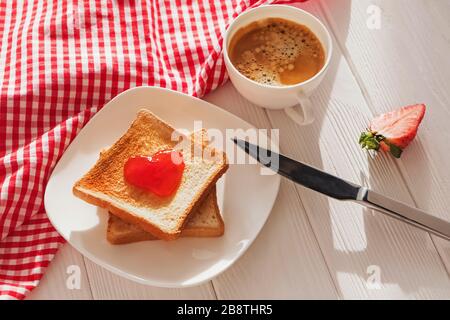 Geröstete Brotscheiben mit herzförmiger Marmelade darauf und einer Tasse Kaffee Stockfoto