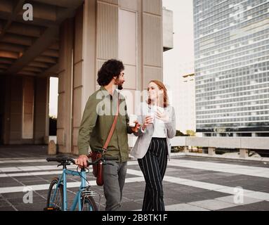 Geschäftsmann mit Fahrrad- und Schleudertasche, die mit einer Frau läuft, die eine Einweg-Kaffeetasse hält Stockfoto