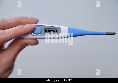 Weibliche Hand hält klinisches Thermometer mit Korona-Text auf dem Bildschirm während der globalen Kovid 19- oder Corona-Pandemie. Stockfoto