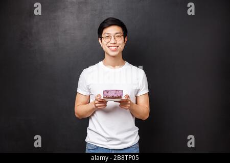 Portrait des fröhlichen fürsorglichen, gutaussehenden asiatischen Freundes bringt ein Stück leckeren Kuchen für die Freundin, versucht, sich zu kümmern und macht einen schönen, schönen Gesten-Express Stockfoto