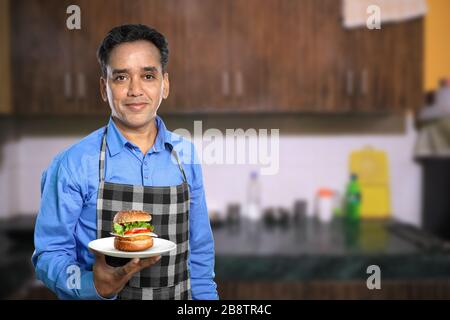 Indischer Küchenchef mit Burger in einer Küche Stockfoto