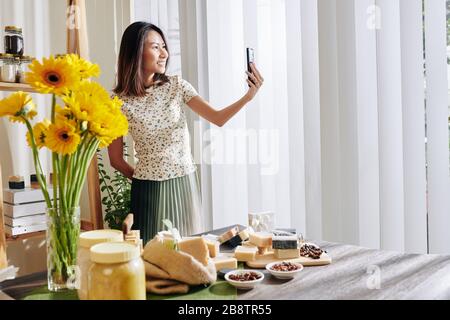 Schöne junge Asiatin, die selfie nimmt, nachdem sie zu Hause duftende Seifenbars gemacht hat Stockfoto