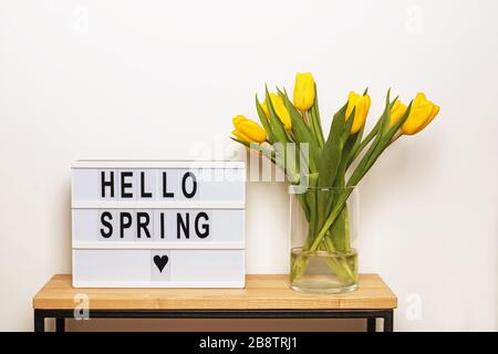 Hallo Frühling Text auf einem Leuchtkasten mit gelben Tulpen Stockfoto