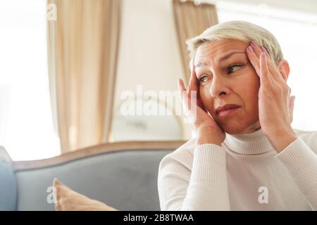 Traurige ältere Dame, die an Kopfschmerzen leidet Stockfoto