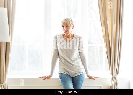 Fröhlich-ältere Frau sitzt auf dem Sill Stockfoto