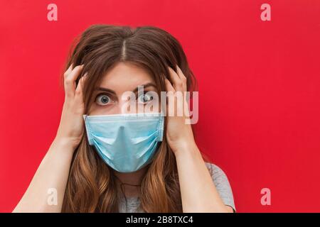 Verängstigte junge Frau in medizinischer Maske, die über rotem Hintergrund steht. Stockfoto