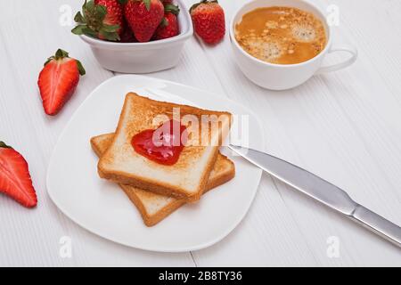 Frische Toasts mit Erdbeermarmelade in Herzform, Kaffee und Erdbeeren Stockfoto