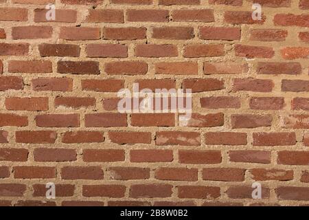Detail der Textur, beleuchtet durch Nachmittaglicht, die die Reihen von rötlichen Ziegelsteinen einer der Wände des Conde Duque Kulturzentrums bilden. Stockfoto