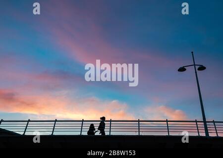 Mutter und Tochter, die bei Sonnenuntergang an einer Brücke in Valencia, Spanien, spazieren gehen Stockfoto