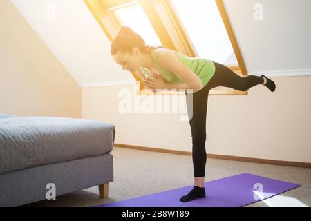 Junge Frau übt zu Hause Yoga aus. Warrior Pose / Virabhadrasana Stockfoto