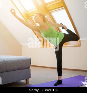 Junge Frau übt zu Hause Yoga aus. Natarajasana/Shiva-Haltung posieren Stockfoto