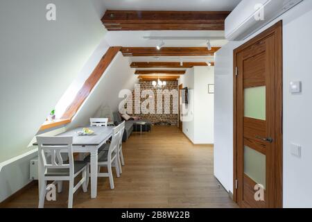 Modernes Holz-Loft im Inneren des Apartments. Gemütliches Sofa und Fernseher. Privathaus. Mauer aus Backstein. Tisch und Stühle. Stockfoto