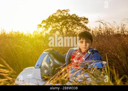 Der junge Junge wagt mit seinem Spielzeugauto in ländlicher Umgebung bei Sonnenuntergang in die Welt Stockfoto