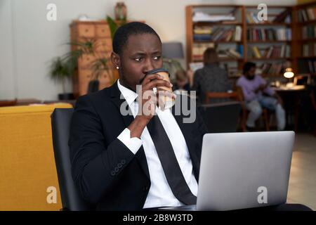afroamerikanischer Geschäftsmann mit Kaffee auf dem Laptop in einem Hotel Stockfoto