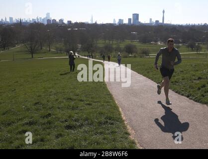 Die Skyline von London liegt in der Ferne hinter den Besuchern von Primrose Hill, London. Premierminister Boris Johnson sagte, die Regierung sei bereit, härtere Einschränkungen zu verhängen, um die Ausbreitung des Coronavirus einzudämmen, wenn die Menschen nicht den Leitlinien für soziale Distanzierungen folgen. Stockfoto