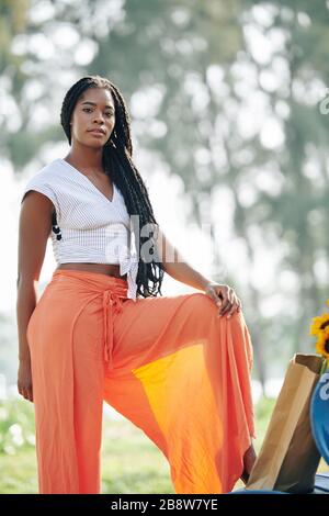 Schöne seriöse junge Frau, die im Freien in einer breiten orangefarbenen Leinenhose posiert Stockfoto