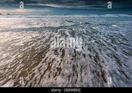 Eine sich zurückziehende Ebbe an einem kalten kühlen Abend am Fistral Beach in Newquay in Cornwall. Stockfoto