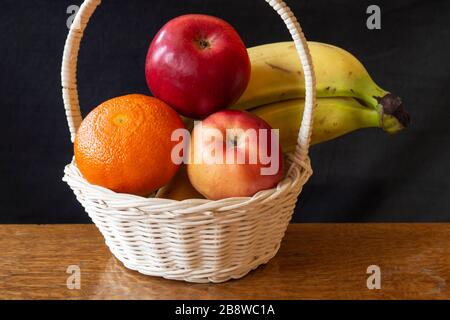 Die Früchte in hellem Korb auf Holztisch.Apfel, Bananen und Tangerine auf dunklem Grund Stockfoto