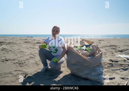 Frau holt Müll vom Strand in Müllsäcken Stockfoto