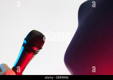Nahaufnahme der Frau, die ein blau-rot beleuchtetes Stimmmikrofon auf weißem Hintergrund hält. Musik, Gesang, Disco, Karaoke und Tonwiedergabe. Stockfoto