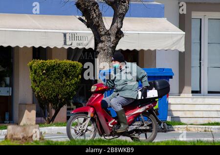 ALEXANDROUPOLI, GRIECHENLAND - 21. März 2020 - EIN Mann auf einem Roller trägt Gummihandschuhe und eine Gesichtsmaske im Zentrum von Alexandroupoli, Griechenland, um ihn zu schützen Stockfoto