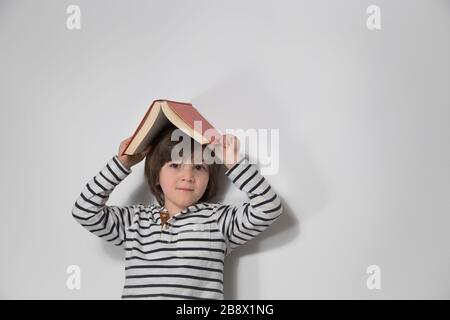 Vorschulter mit rotem Buch auf dem Kopf Stockfoto