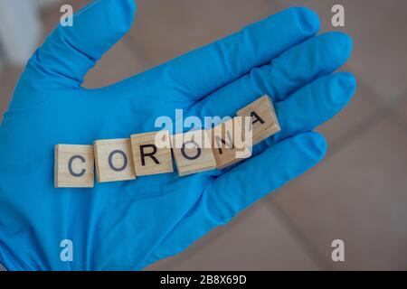 Eine Hand mit einem Handschuh auf hält Scrabble Steine, die das Wort bilden: Corona Stockfoto