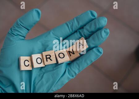 Eine Hand mit einem Handschuh auf hält Scrabble Steine, die das Wort bilden: Corona Stockfoto