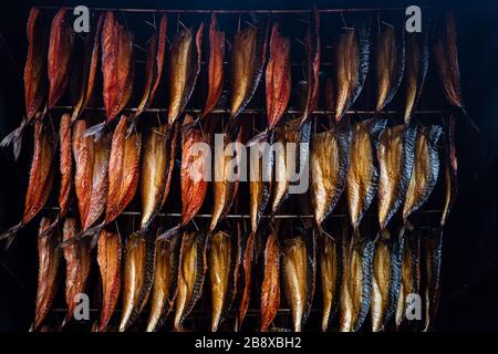 Rauchende Fischfilets hängen in einem Raucher nebeneinander. Kalt geräucherte Makrelenstücke zum Verkauf auf dem Fischmarkt Stockfoto