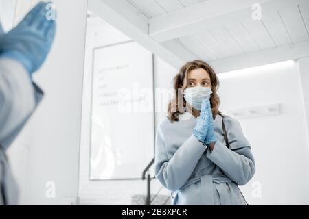 Junge Frau in medizinischer Maske und Handschuhen betet, bevor sie nach draußen geht. Konzept einer Coronavirus-Pandemie und Schutz vor Virusinfektionen Stockfoto
