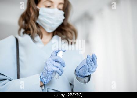 Frau in medizinischer Maske und Handschuhen desinfiziert die Hände, nachdem sie von der Straße nach Hause kam. Konzept der Vorbeugung von Virusverbreitung während einer Epidemie Stockfoto