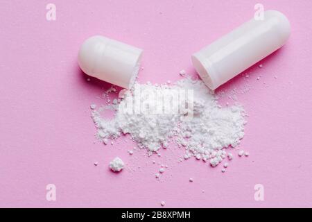 Weißes Pulver, das auf der rosafarbenen Oberfläche verschüttet wurde, bildet eine Drogenkapsel Stockfoto