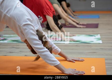 Sportliche Menschen üben Yoga-Unterricht mit Kursleiter, Strecken in Kinderübung auf Matte, Stockfoto