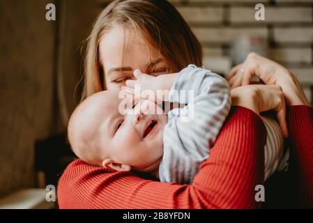 Eine Mutter hält ein Kind in den Armen. Eine Mutter küsst ein Kleinkind. Eine junge Frau umarmt ihren Säugling. Ein Mädchen hat Spaß und freut sich über das Baby.Close up. Stockfoto