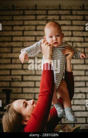 Die Mutter hebt das Kleinkind über ihren Kopf. Die Mutter hebt sich in ihre Hände Baby. Eine junge Frau hat Spaß und freut sich über den Säugling. Stockfoto