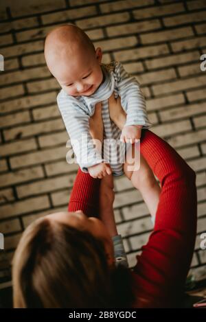 Die Mutter hebt das Kleinkind über ihren Kopf. Die Mutter hebt sich in ihre Hände Baby. Eine junge Frau hat Spaß und freut sich über den Säugling. Stockfoto