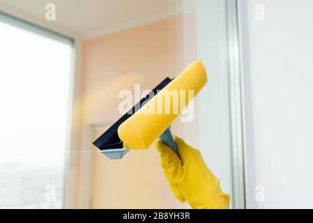 Fensterreiniger zum Waschen von Fenstern. Hand in Gelb Handschuhhalterungs-Reinigungskübel. Reinigen eines Glases mit einem Quiegee, Nahaufnahme. Stockfoto