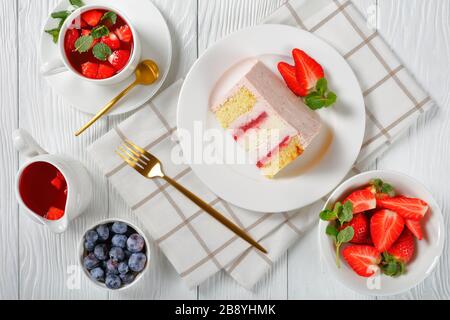 Eine Scheibe eines rosafarbenen Erdbeerchekakes, serviert mit frischen Beeren und Erdbeerlemonade auf einem Holztisch, horizontaler Blick von oben, flacher Lay, Klo Stockfoto