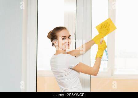 Süßes Mädchen mit aufgesammelten Haaren wäscht ein Glas mit Waschmittel. Ordnung und Sauberkeit und Hausaufgaben. Federreinigung. Schöne Frau Reinigungsfenster zu Hause. Stockfoto