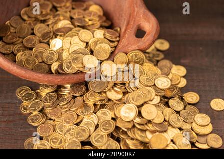 Kaskade kleiner goldener Münzen aus einem Terrakotta-Topf Stockfoto