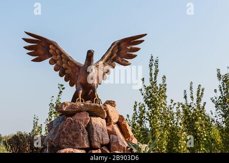 Katta Turk, Usbekistan - 18. Oktober 2019: Statue eines Adlers mit ausgebreiteten Flügeln auf den Steinen auf der Seite der Straße im Stadtteil Dangara Stockfoto