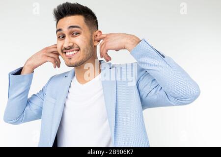 Der Mann in einer blauen klassischen Jacke steckt seine Ohren mit den Fingern vor lauten Geräuschen auf weißem Hintergrund Stockfoto