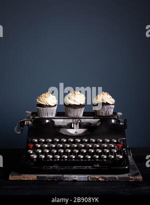 Schokoladenkuchen, mit weißer Creme dekoriert, die auf alter alter Vintage-Schreibmaschine auf dunklem Hintergrund stehen. Freier Speicherplatz für Ihren Text Stockfoto
