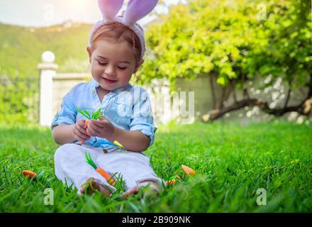 Kleiner Junge mit Freude an den Osterfeiertagen, mit lustigen, gruseln Hünenohren, der sonnige Tag auf dem Hinterhof genießt, glücklicher Frühlingsurlaub Stockfoto