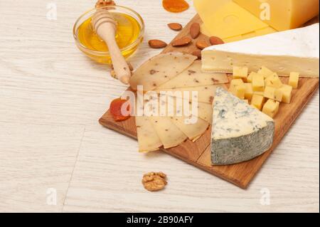 Verschiedene Käsesorten mit Nüssen und getrockneten Aprikosen und Honig auf einem Holzbrett. Draufsicht Stockfoto